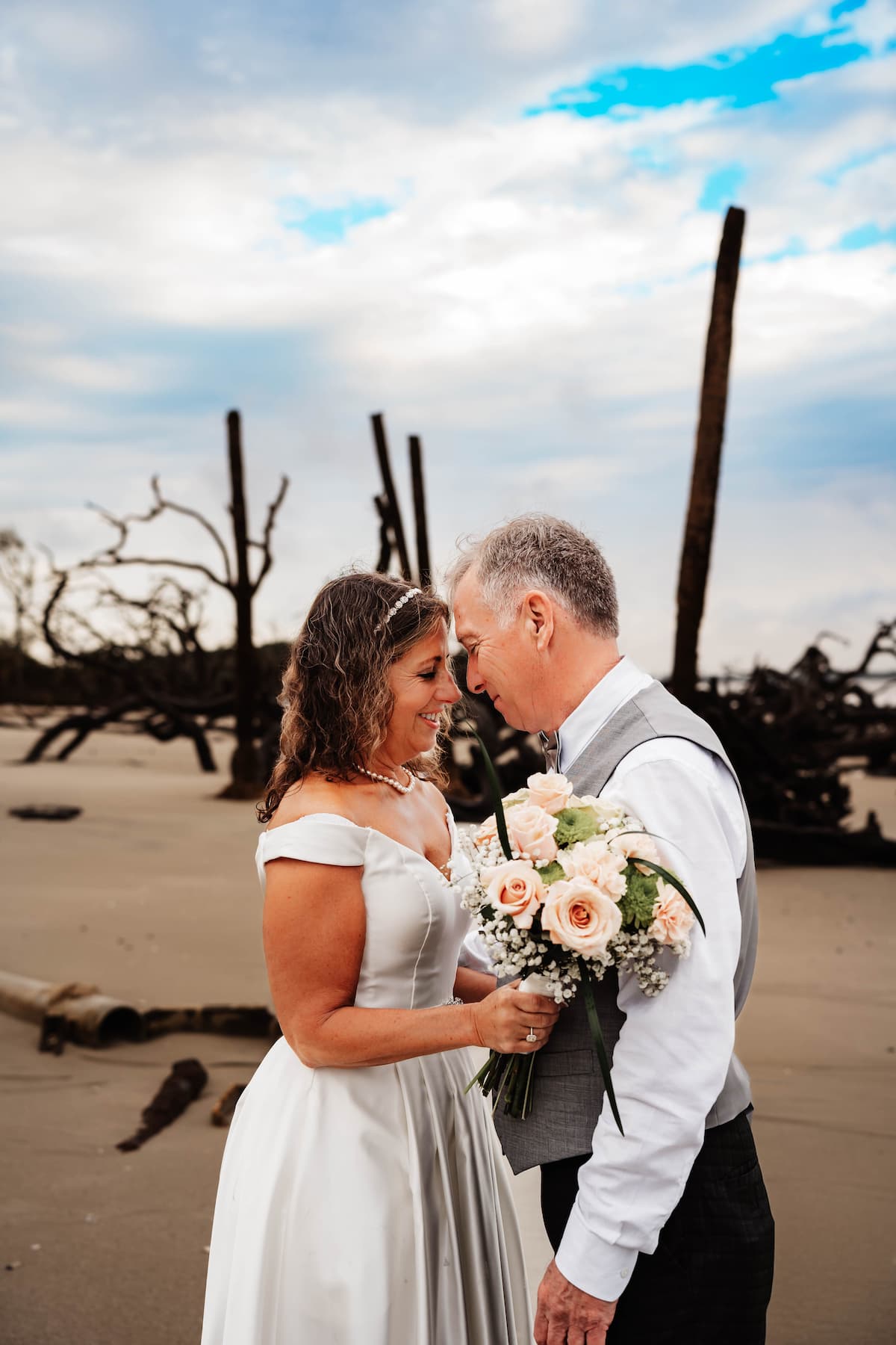 Bride and groom standing on beach holding bouquet 