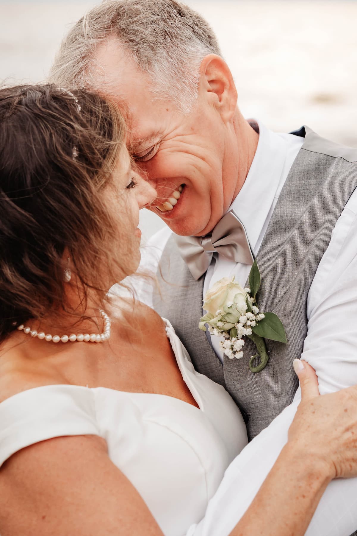 groom holding bride close on beach