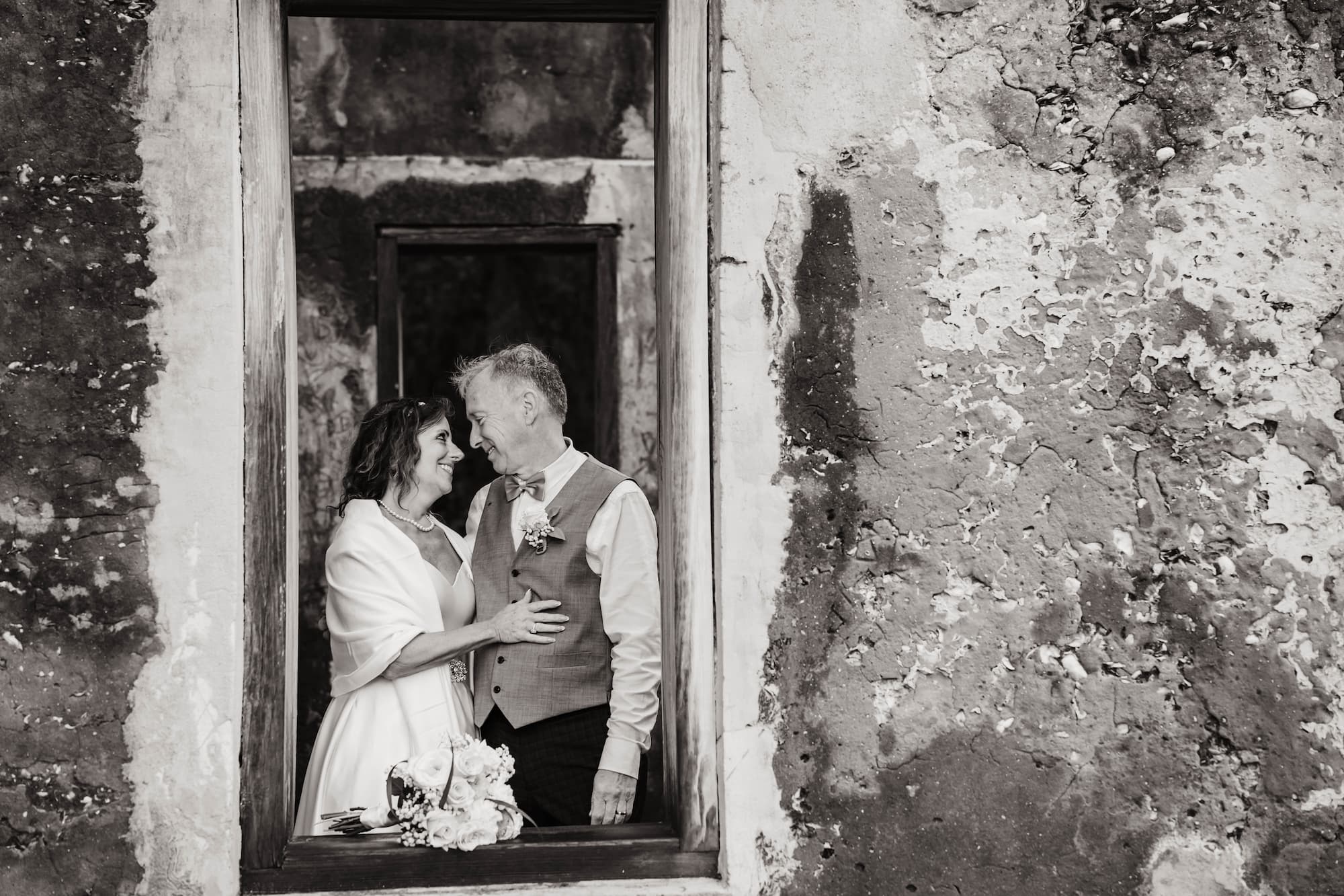 Bride and groom standing in rustic building window