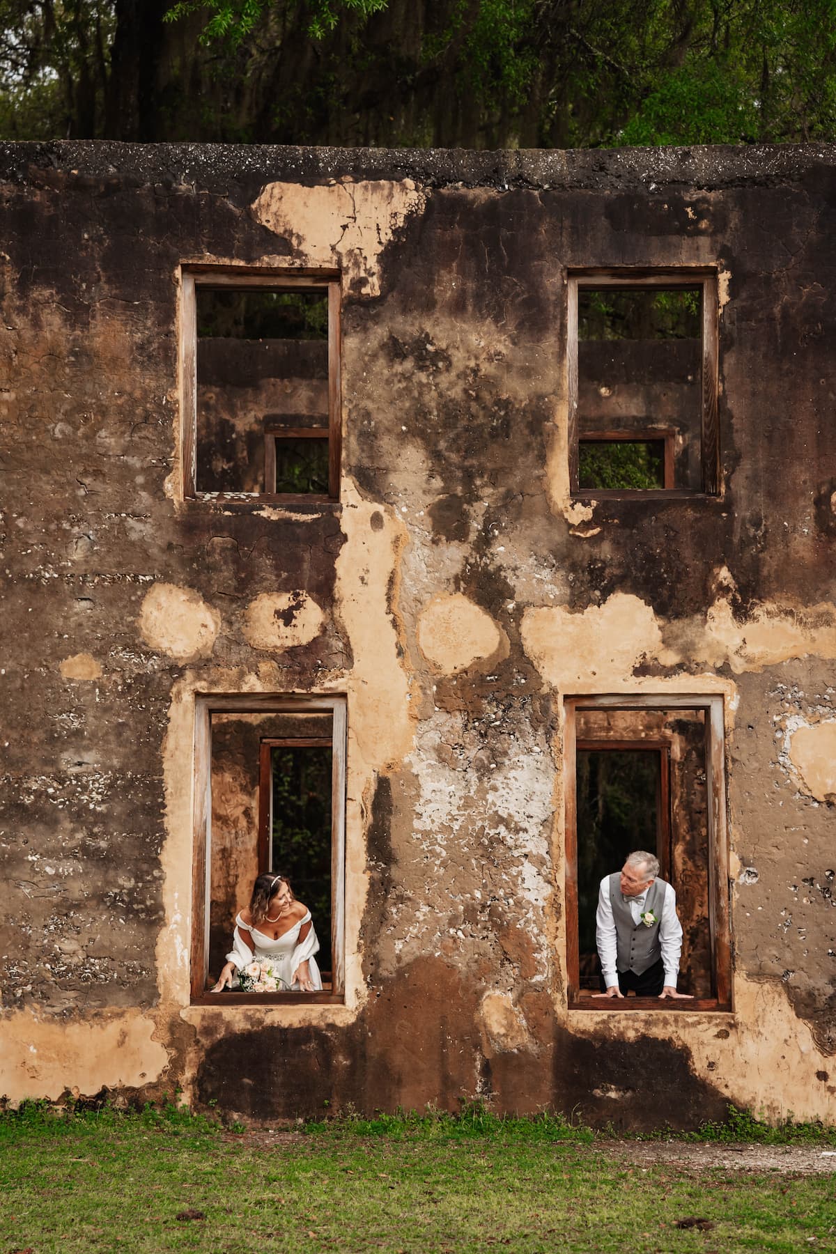 Bride and groom in rustic building looking out windows at each other